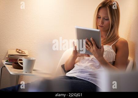 Selecting a new ebook to read - Digital tablet. Attractive young woman using her tablet in an armchair at home. Stock Photo