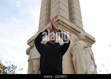 A young and handsome man dancing flamenco on a street, dressed in black, wearing red shoes, in front of a monument in Spain Stock Photo
