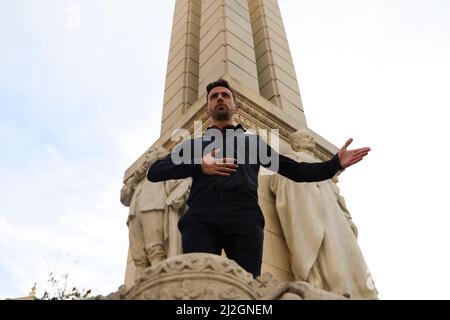 A young and handsome man dancing flamenco on a street, dressed in black, wearing red shoes, in front of a monument in Spain Stock Photo