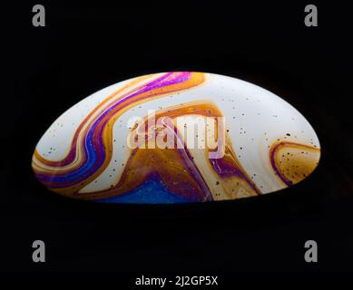 A close-up shot of a rainbow soap bubble in a dark background. Stock Photo