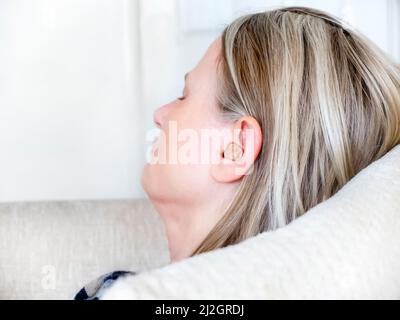 Female taking a break from work,listening to a language learning app,relaxing on the sofa with her eyes closed,in her living room,connected wirelessly Stock Photo