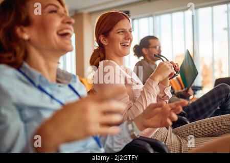 Two cheerful female colleagues having fun during a business lecture in a pleasant atmosphere in the conference room. Business, people, company Stock Photo