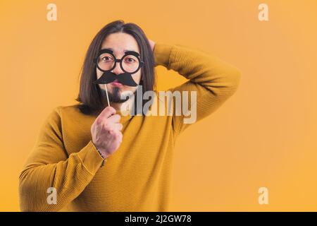 Funny disguise concept. Adult caucasian man wearing fake glasses and mustache over yellow background. High quality photo Stock Photo