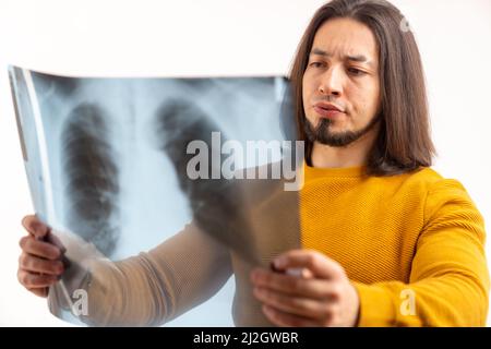 Studio shot of a confused worried bearded man with long hair holding his lungs x-ray to the camera. High quality photo Stock Photo