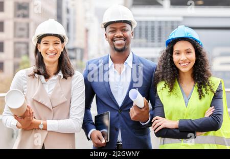 Were here to build. Cropped portrait of three young engineers standing with blueprints on a construction site. Stock Photo