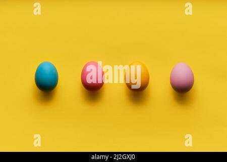 four colorful easter eggs in a row on yellow paper with plenty of copy space Stock Photo