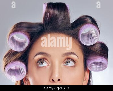 Please be perfect waves. Cropped shot of an attractive young woman standing alone in the studio and posing with rollers in her hair. Stock Photo