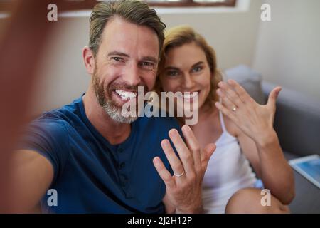 Look who just got married. Shot of a happy middle aged couple taking a selfie and showing off their wedding rings at home. Stock Photo
