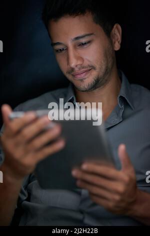 Whats the latest on social media. Cropped shot of a young man using his tablet at night. Stock Photo