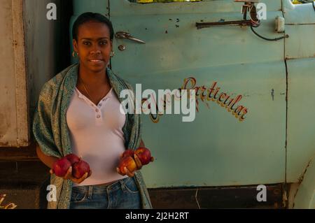 Cuban woman holding apples in front of an old truck w/ Spanish writing on the door. Havana, Cuba. credit: Kraig Lieb Stock Photo
