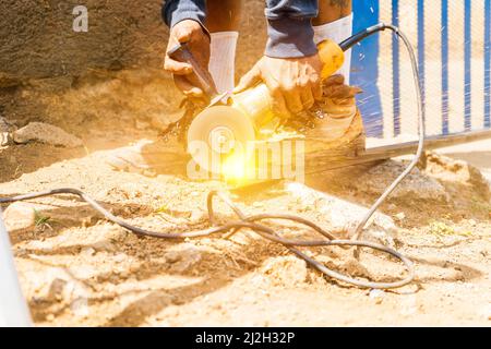 Closeup of the hands of a latin blue collar worker using a handheld circular saw to cut a tube Stock Photo