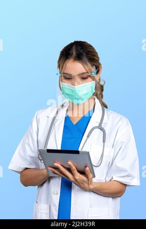 Isolated photo of female doctor in uniform with mask and face shield working on digital tablet in hands. Stock Photo