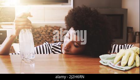 Shes been cleaning the whole day. Shot of a tired young woman resting her head on a table after trying to clean it with cleaning equipment at home Stock Photo