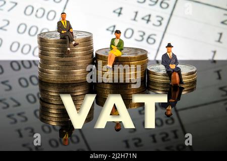 Miniature people: Elderly people sitting on coins stack. Stacks of coins with the letters VAT isolated on white background Stock Photo