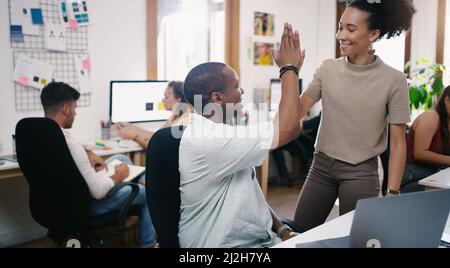 High five for high profit. Shot of a young businessman and businesswoman giving each other a high five while using a laptop in an office. Stock Photo