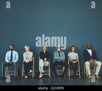 Consider everything a test, even the possible extended 10-minute wait. Shot of a group of well-dressed business people seated in line while waiting to Stock Photo