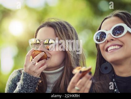 Everythings just peachy. Cropped shot of two attractive young women eating a peach while sitting in the park. Stock Photo