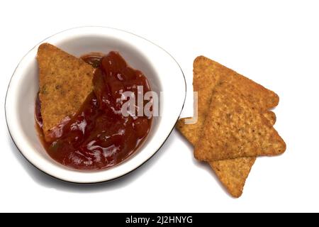 Close up of triangular tortilla chips stacked next and one in ceramic bowl with salsa dipping sauce on white background concept for Mexican spicy fier Stock Photo