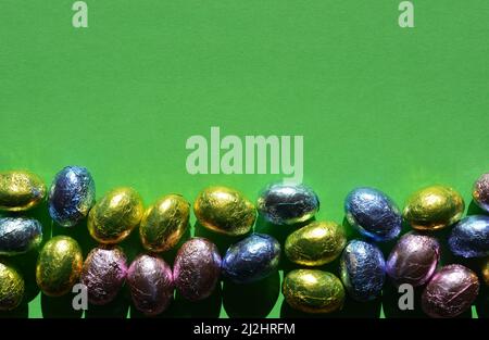 Foil wrapped chocolate Easter eggs isolated on bright green background with copy space Stock Photo