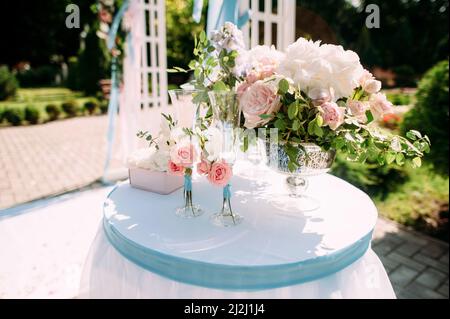 Wedding ceremony details in pink and blue. White wedding arch, natural flowers decorations, champagne glasses on green background. Bright summer weddi Stock Photo