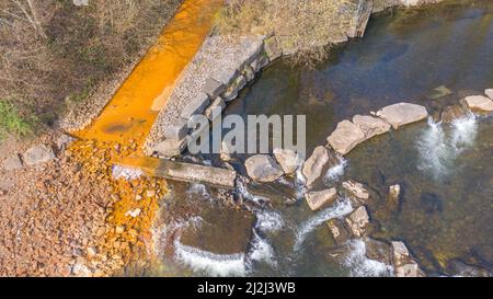 Aerial view of orange iron oxide staining in stream entering River Neath at Abergarwed. The source is water discharging from an abandoned coal mine. Stock Photo