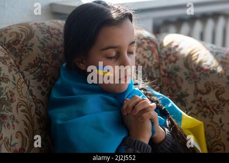 the face of a frightened girl, a child crying, tears flowing, painted on her cheek in the yellow-blue colors of the Ukrainian flag, a request for help Stock Photo