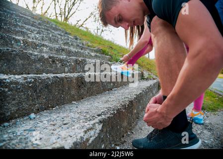 Getting ready for jogging. African sporty woman in black sportswear tying shoelaces before run with boyfriend or friend in the park Stock Photo