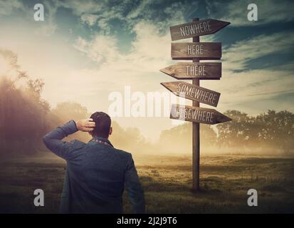 Lost and confused businessman in front of a signpost showing impossible directions. Business dilemma and difficult choice concept. Choosing the correc Stock Photo