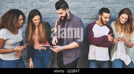 Good friends and a great wifi connection. Shot of a group of young friends using their wireless devices together outdoors. Stock Photo