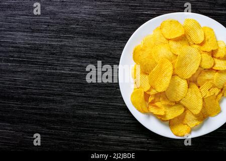 Potato chips chips in a white plate on a wooden table. Rustic food background. Top view. Copy space Stock Photo
