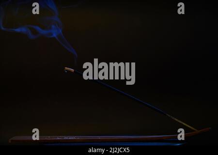 Incense stick with smoke against black background. Stock Photo
