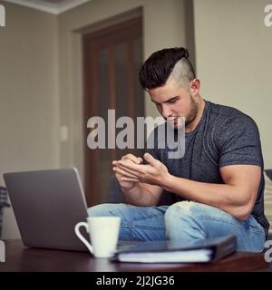 Memo remember to buy a notebook. Shot of a serious young man making notes on his hand while he works on his laptop at home. Stock Photo