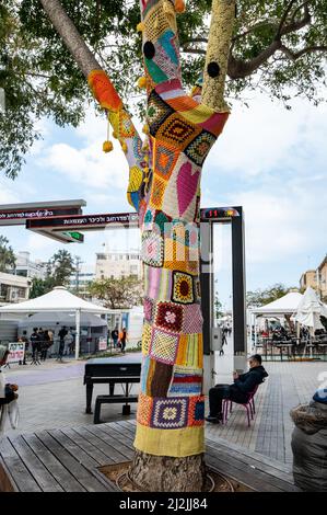 Netanya, Israel - February 7, 2022: Colorful crochet knit on a tree trunk yarn bombing. Patchwork knitted crochet covered tree for warmth, protection Stock Photo