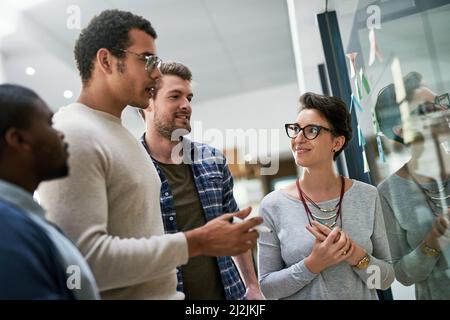We have to plan together to plan better. Shot of a group of designers brainstorming with notes on a glass wall in an office. Stock Photo
