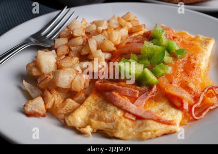 Omelette with cheese, red tomato and onion spicy salsa and cubes of green peppers on top with a side of squared deep fried potatoes Stock Photo