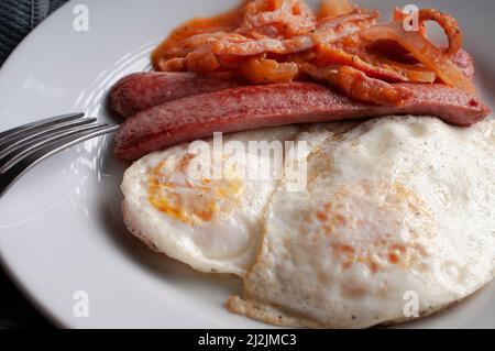 well done fried eggs with sausage and tomato and onion spicy salsa on a white plate Stock Photo