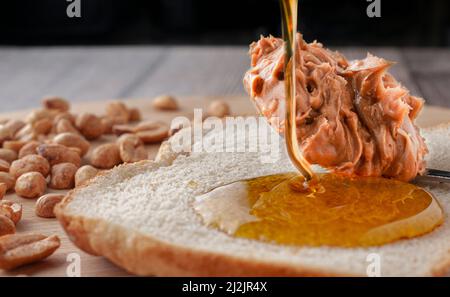 Honey falling on a slice of bread and a spoon of peanut butter, with peanuts in the background. Macro photography, horizontal format. Stock Photo