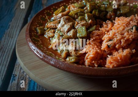 Pork. Mexican food, chicken with nopales and mexican rice with hand made corn tortillas on a mud or clay plate, on a wooden round cutting board. Stock Photo