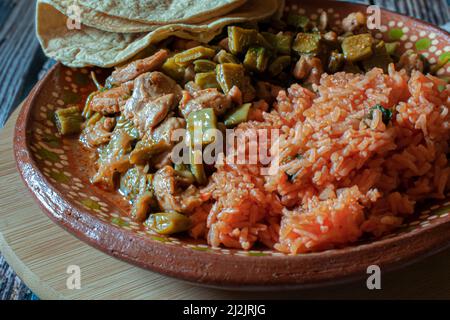 Pork. Mexican food, chicken with nopales and mexican rice with hand made corn tortillas on a mud or clay plate, on a wooden round cutting board. Stock Photo