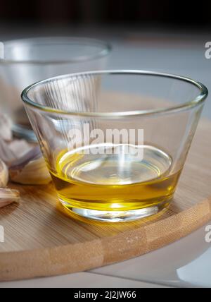 A glass with olive oil with garlics and black pepper on a cutting board as part of kitchen ingredients, Macro photography. Stock Photo