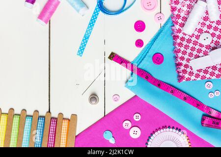 Various pink and blue fabric, tools and accessories for sewing on a light wooden background. Top view, copy space. Stock Photo