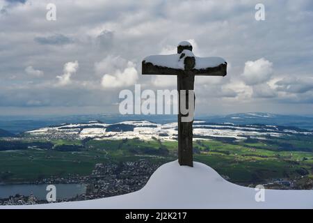 Snow-covered crucifix in mountains and view from Seebodenalp, Schwyz, Switzerland Stock Photo