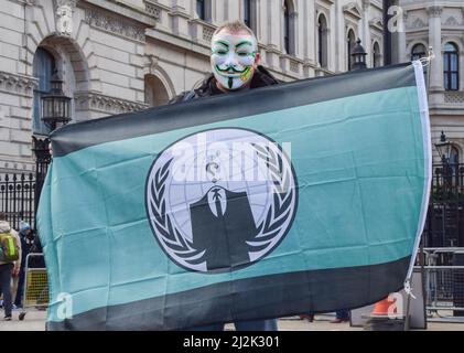 London, England, UK. 2nd Apr, 2022. A protester wearing a mask holds a flag from the hacktivist group Anonymous. Hundreds of people gathered outside Downing Street in protest against the rise in energy costs, the cost of living crisis, and the Tory Government. (Credit Image: © Vuk Valcic/ZUMA Press Wire) Credit: ZUMA Press, Inc./Alamy Live News Stock Photo