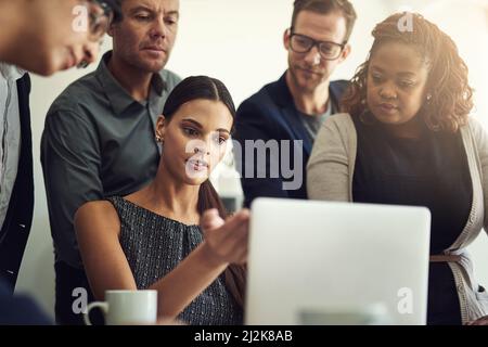 They are talented professionals with a shared vision. Shot of a group of coworkers discussing something on a laptop during a meeting. Stock Photo