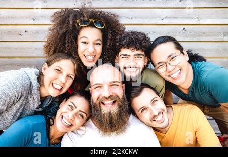 Multicultural guys and girls taking selfie outdoors on wooden background - Happy milenial life style concept with young multiethnic hipster people hav Stock Photo