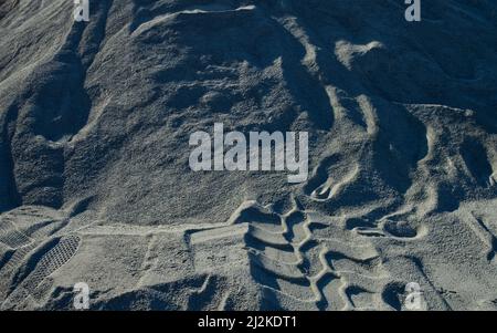 traces of upward shoe prints and skid marks in grey sand Stock Photo