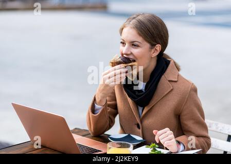 young student eating a mouth-watering chocolate muffin, business woman having a break sitting at the table of a bar with sweeties and orange juice, re Stock Photo