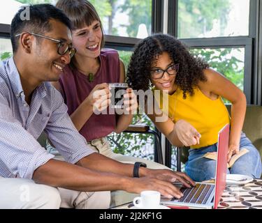 Image of happy young people using laptop while sitting at cafe, young african american woman pointing device, multiethnic group of students in a coffe Stock Photo