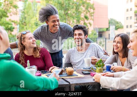 group of multiethnic friends having breakfast with coffee, cappuccino and chocolate muffin, meeting of young people outdoors at a coffee shop Stock Photo