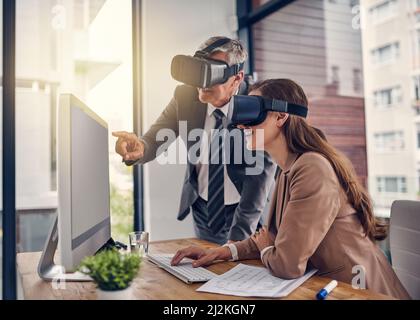 Transferring their ideas through new dimensions. Shot of two businesspeople wearing VR headsets while working on a computer in an office. Stock Photo